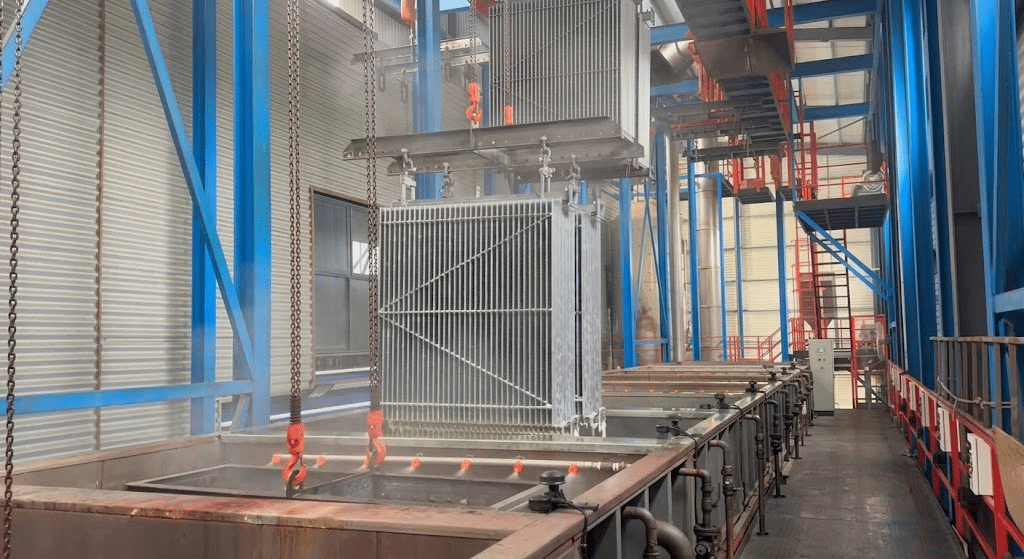 Overhead hoist transferring a radiator-panel transformer tank along the immersion pretreatment line phosphating baths